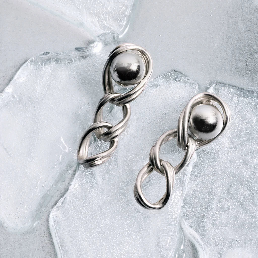 Boucles d’oreilles perles pendantes en métal satiné argenté, posées en nature morte sur un fond de glaçons avec perles.