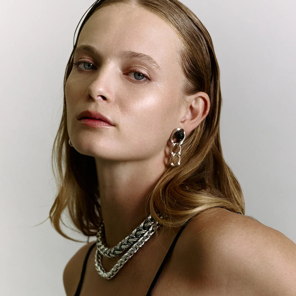 Femme portant des boucles d’oreilles perles pendantes Anomalie en métal satin argenté avec perles noires et deux colliers.