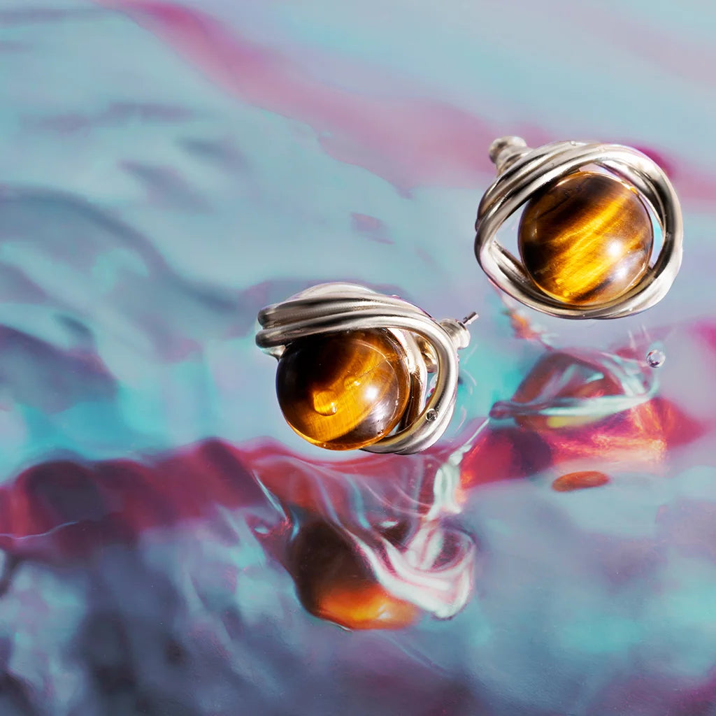 Des boucles d’oreilles perles Anomalie pour femme en métal satiné doré et perles œil de tigre, en nature morte colorée.