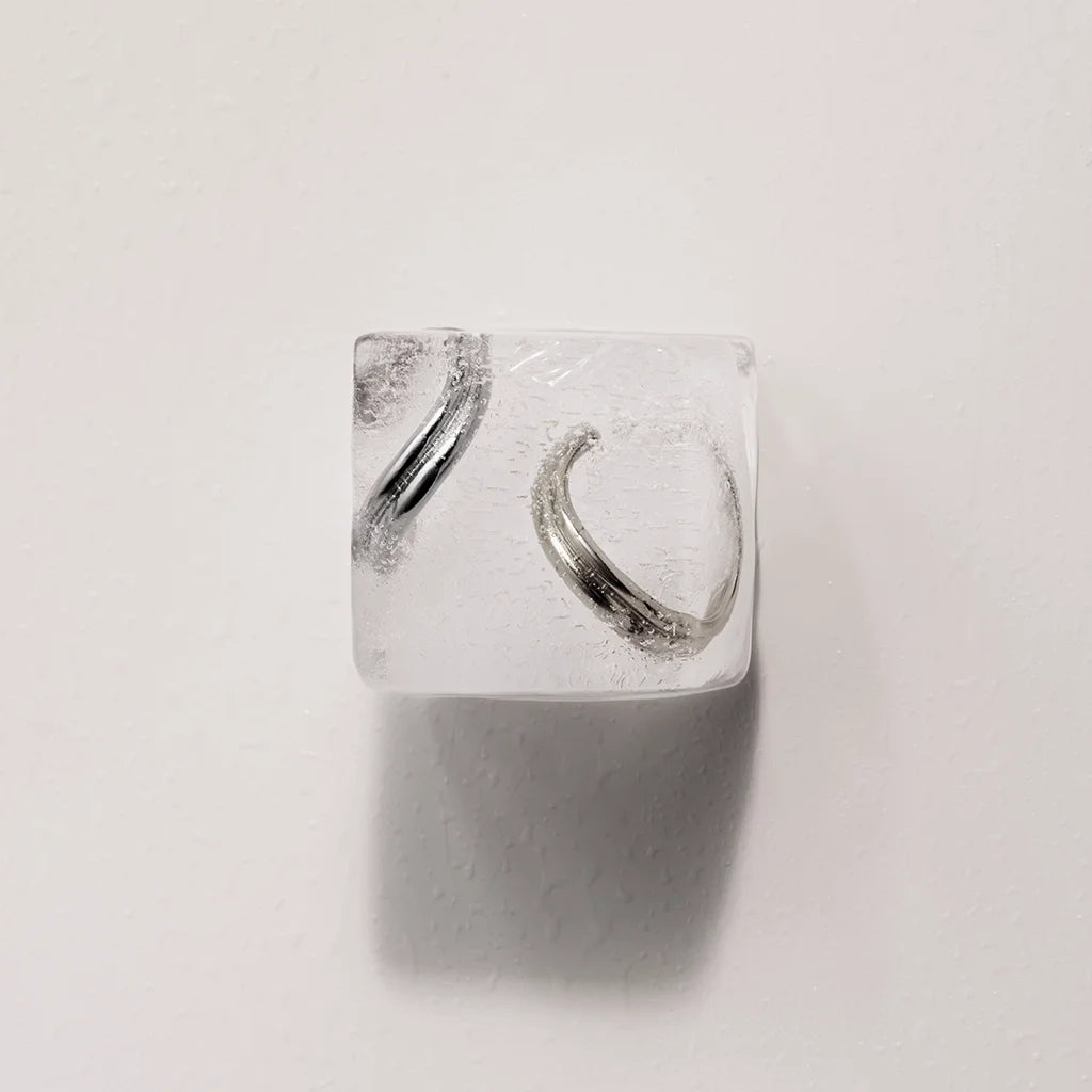 Deux bijoux d’oreilles Anomalie en métal argenté et doré, esthétiquement présentés en nature morte sur un glaçon.