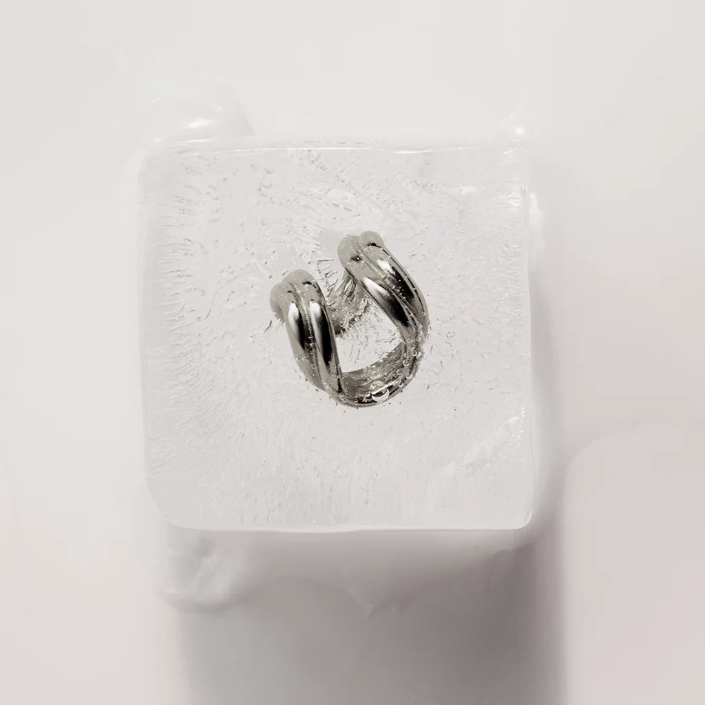 Un anneau d’oreille Anomalie en métal argenté, graphique, entièrement présenté en nature morte sur un glaçon.