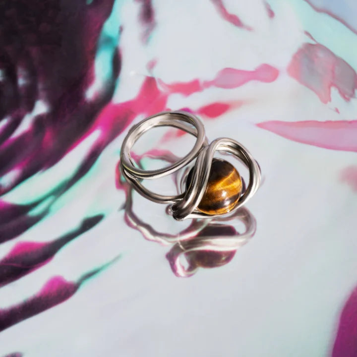 Une bague perle Anomalie en métal satin doré et perle en œil de tigre en nature morte colorée.