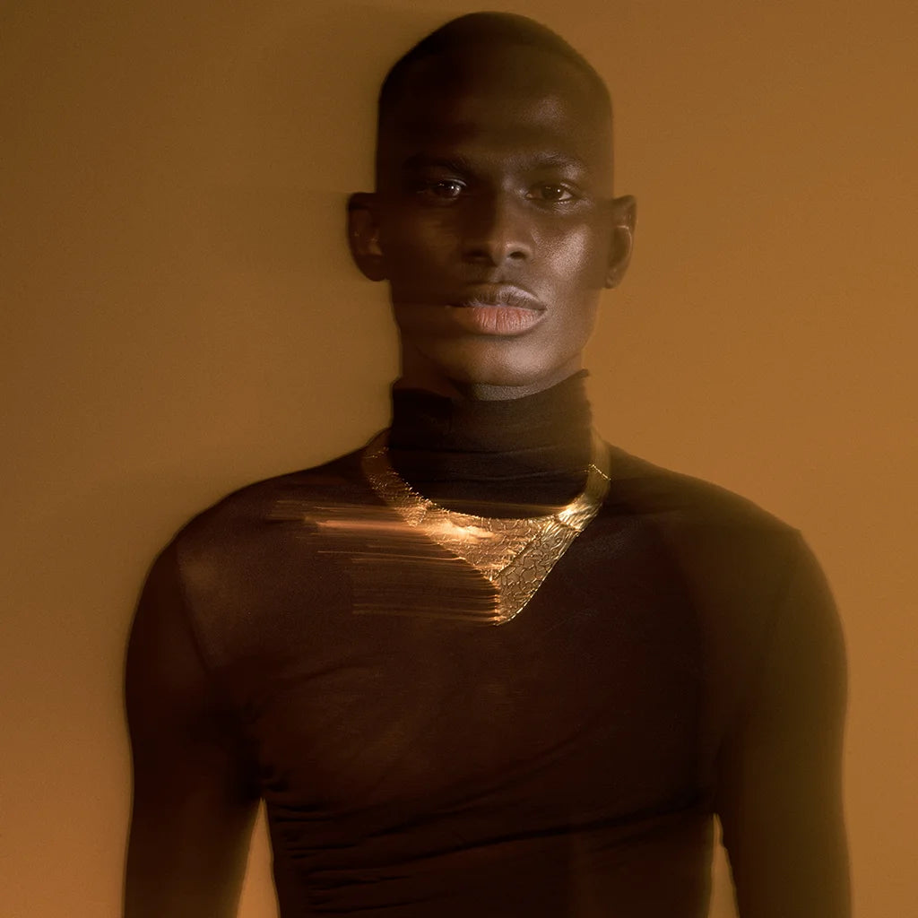 Un homme portant un collier torque Turbulence en vieux doré, à structure rigide en métal avec motifs texturés vieillies.