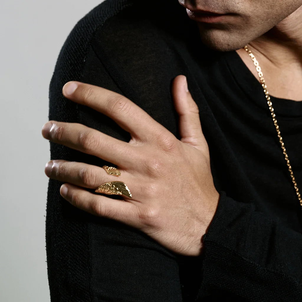 Un homme portant une bague aile Trouble en doré, ouverte aux lignes asymétriques, en motif emblématique l'aile.