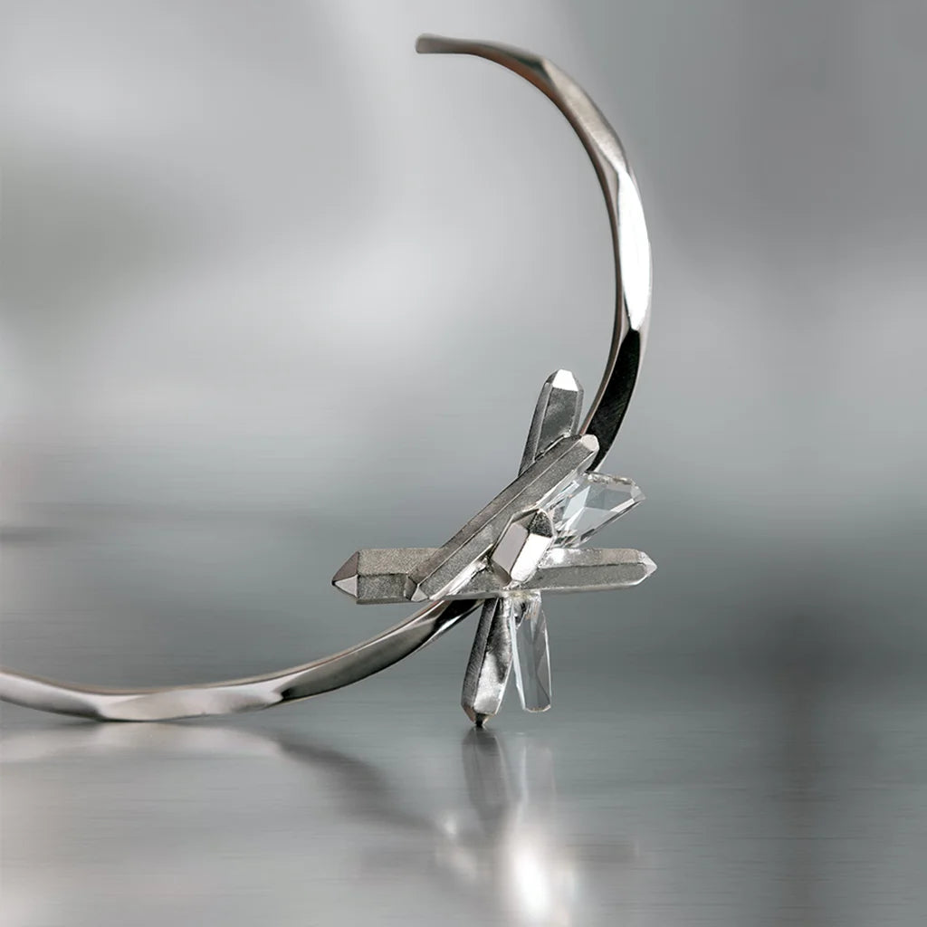Collier torque Turbulence en cristal de roche, métal satiné argenté, en nature morte sur fond aluminium.