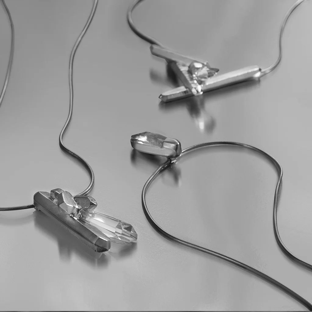 Nature morte présentant un collier cristal, pendentif cristal de roche, et un petit collier Turbulence en métal argenté.