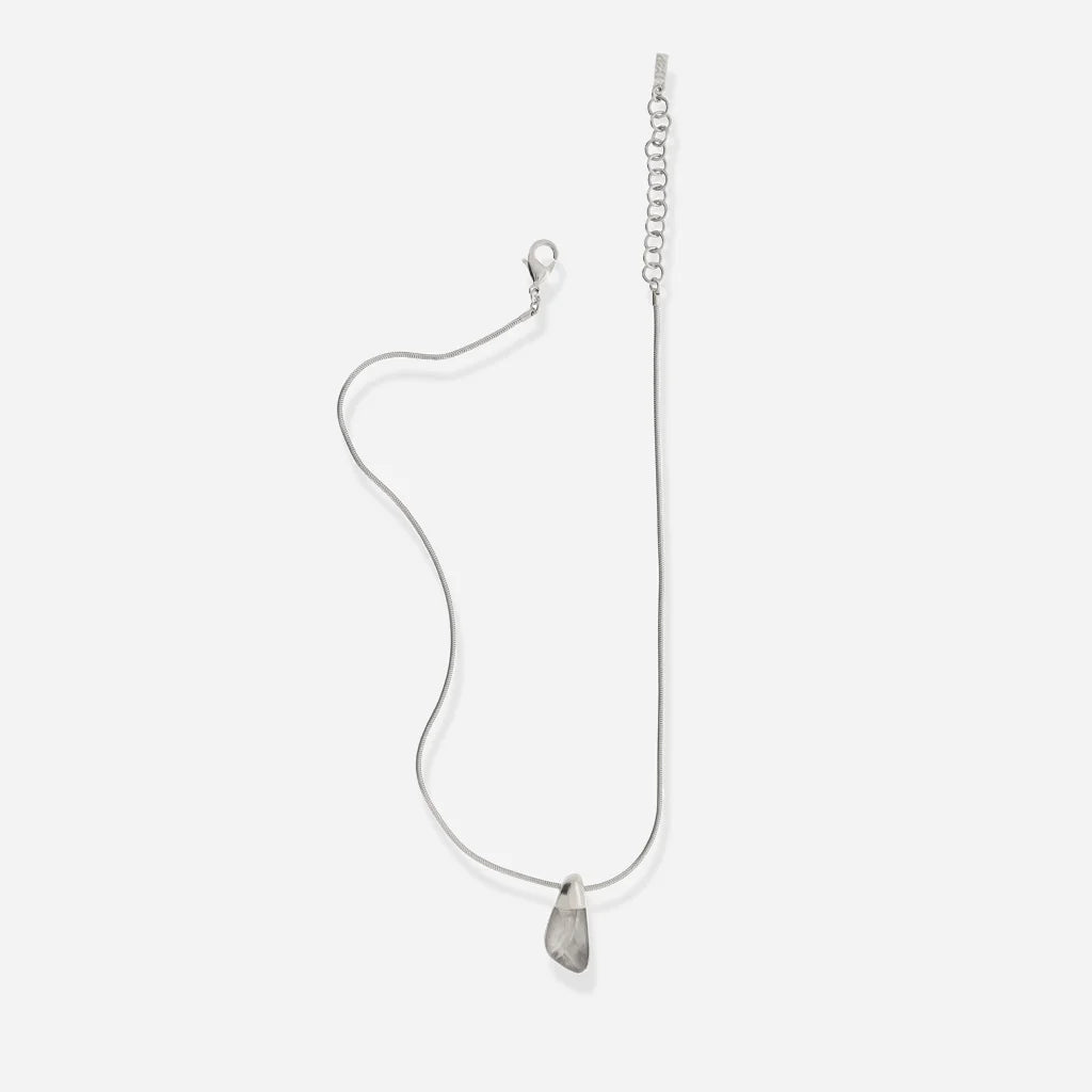 Le petit collier Turbulence en métal argenté révèle son pendentif aux contours irréguliers et sa chaîne fine.