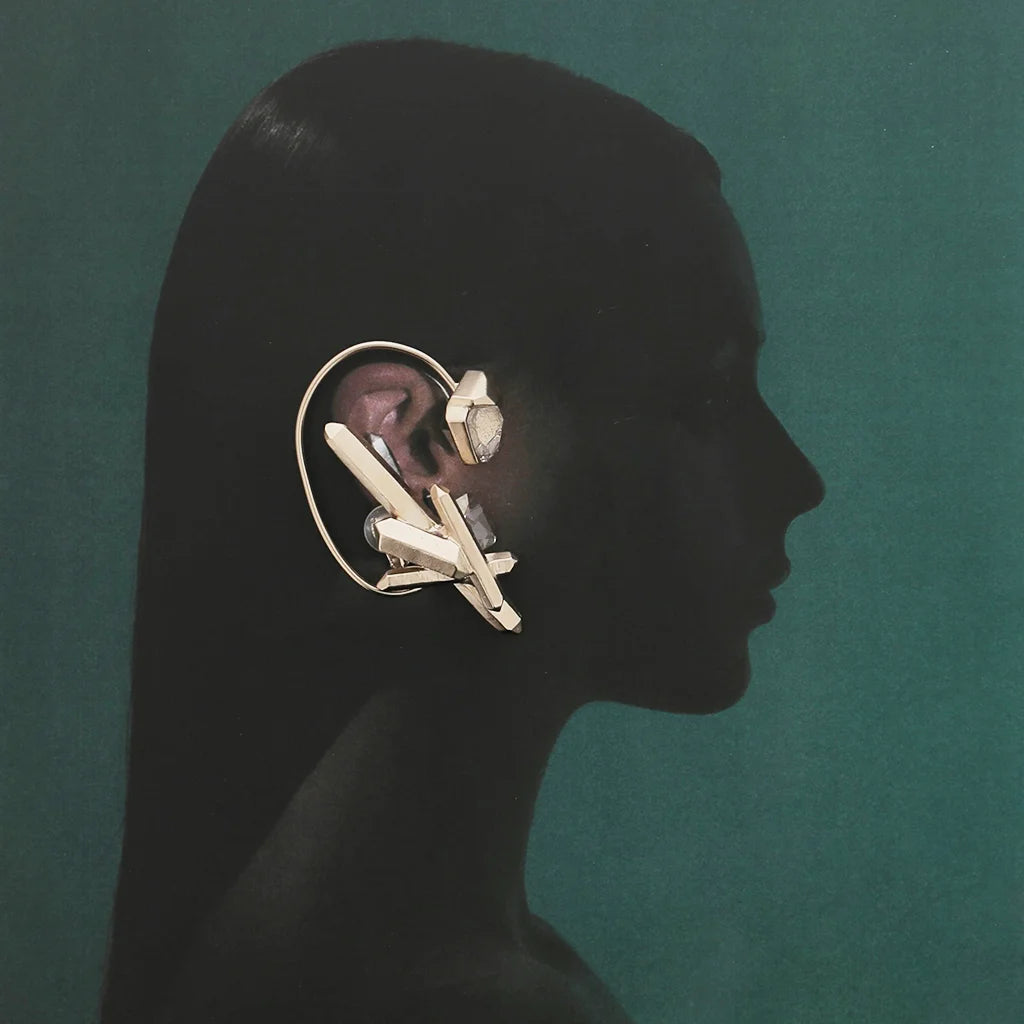Femme de profil portant le bijou d'oreille Turbulence en métal doré, glissant derrière l’oreille sans perçage.