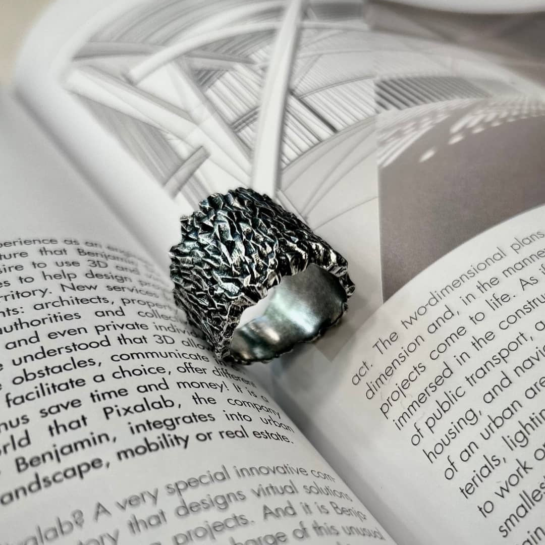 Une large bague jonc Mars en métal satin vieil argenté posé en nature morte sur un livre.