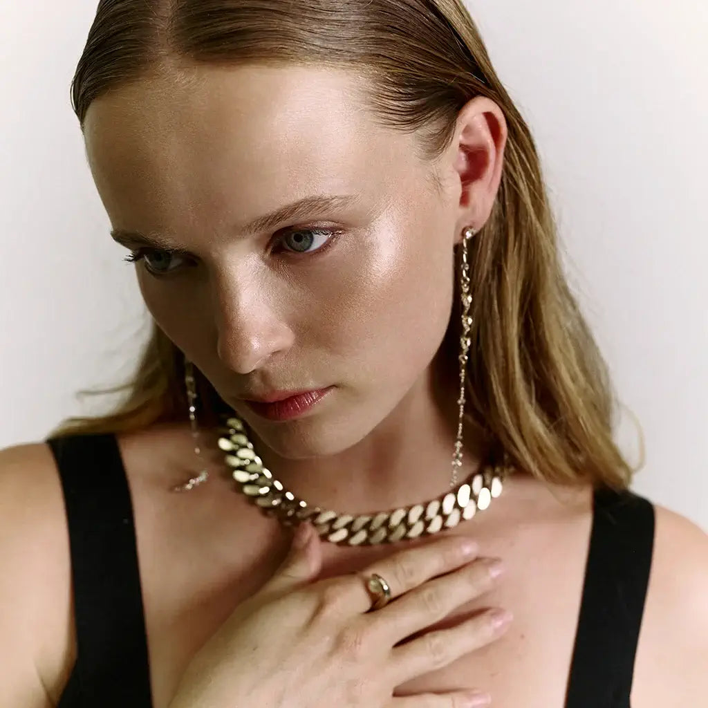 Femme portant les boucles d’oreilles longues pendantes Alex en métal doré, chaînes tressées et strass, associées à la bague perle Noé.