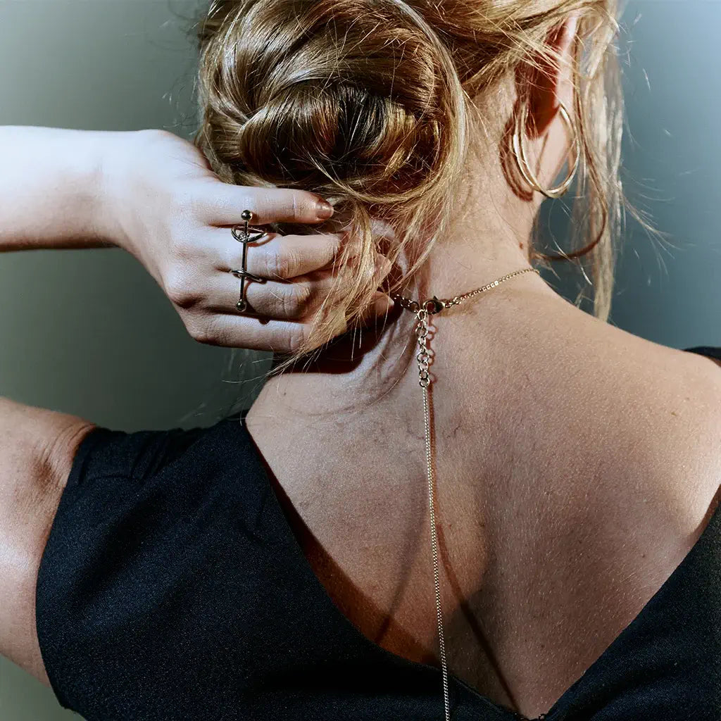 Une femme de dos, sa main portant une bague bicolore avec fibule Balem en métal argenté et doré.