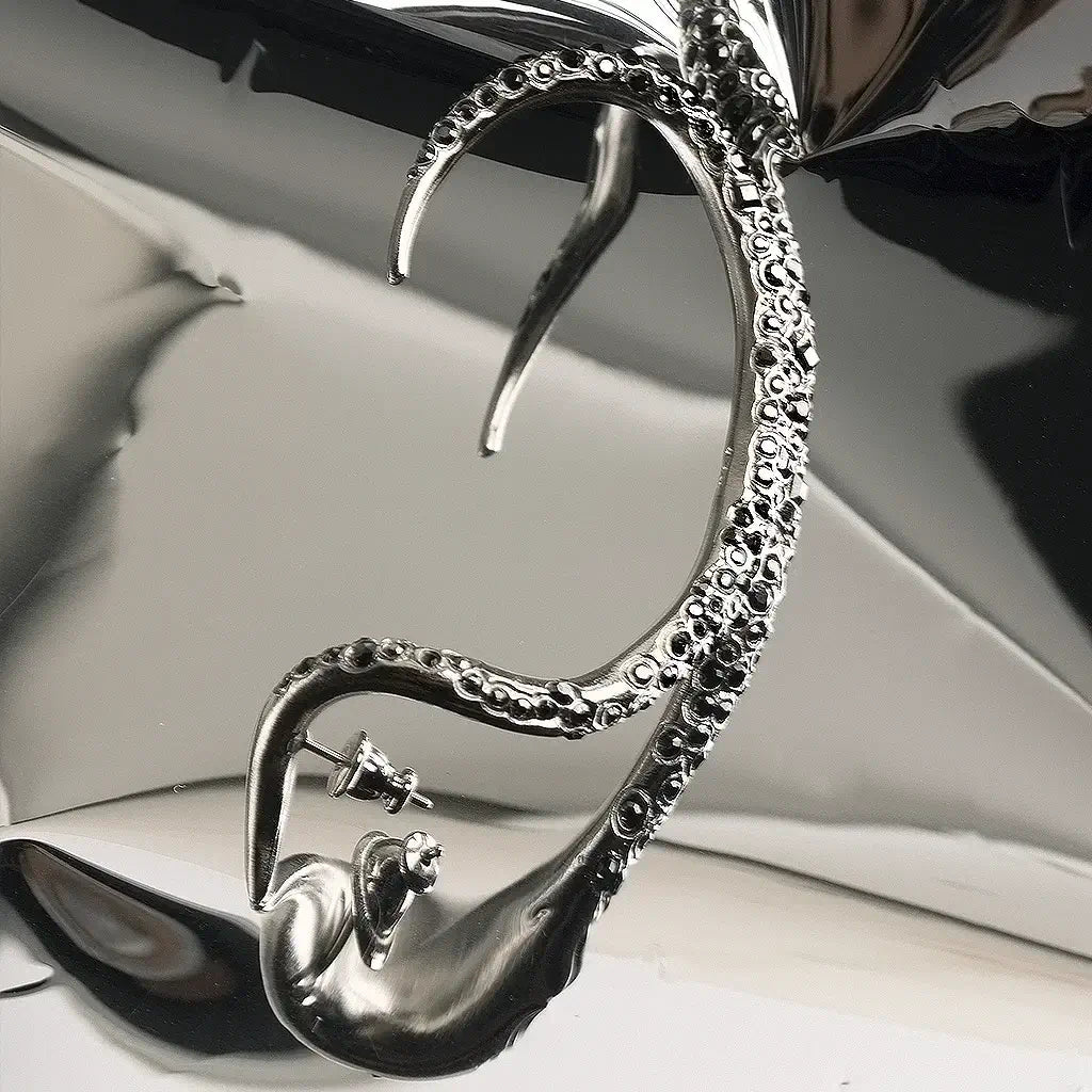 Une boucle d'oreille serpent N°26 en métal satin argenté ornée de strass noirs sur un fond gris.