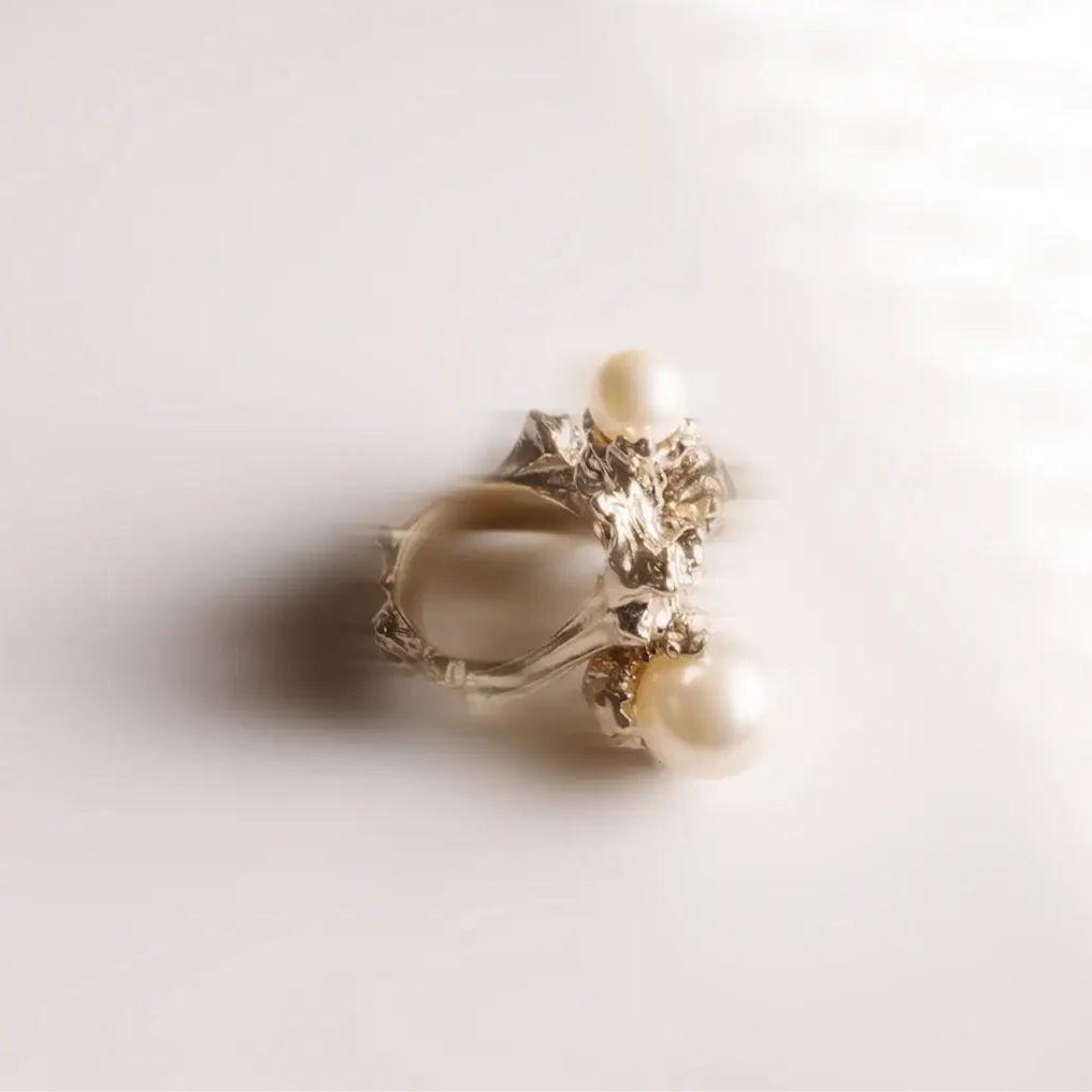 Bague perle Nature en métal doré, ornée de deux perles en cristal laqué, photographiée en nature morte floutée.
