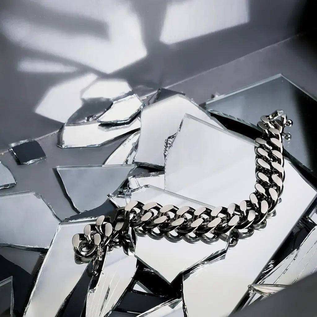 Un bracelet chaîne homme Nebula en métal argenté, posé en nature morte sur un fond gris parsemé d’éclats de verre.