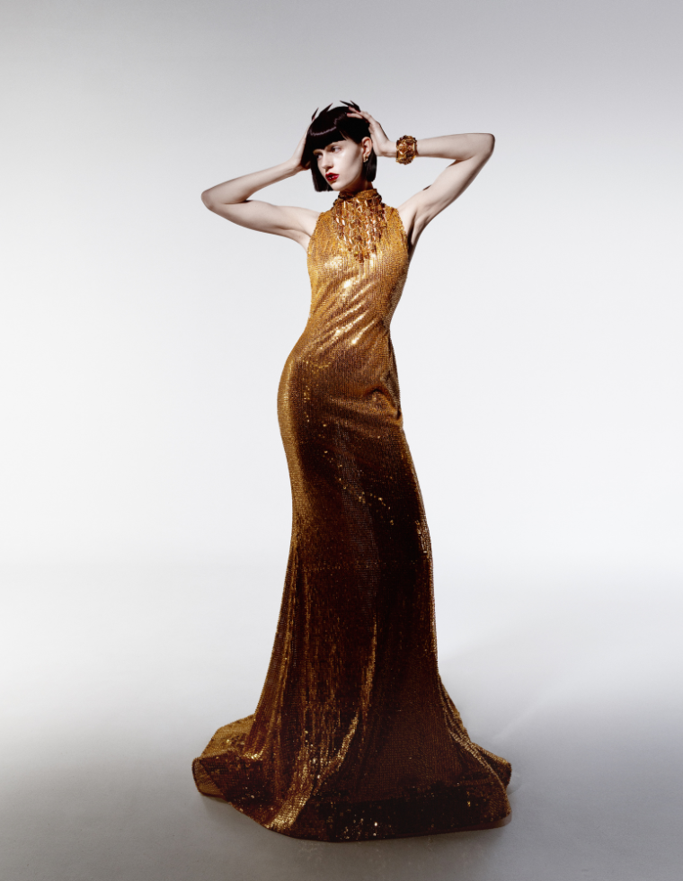 Mannequin portant une robe dorée scintillante et un collier fantaisie doré sur fond clair.