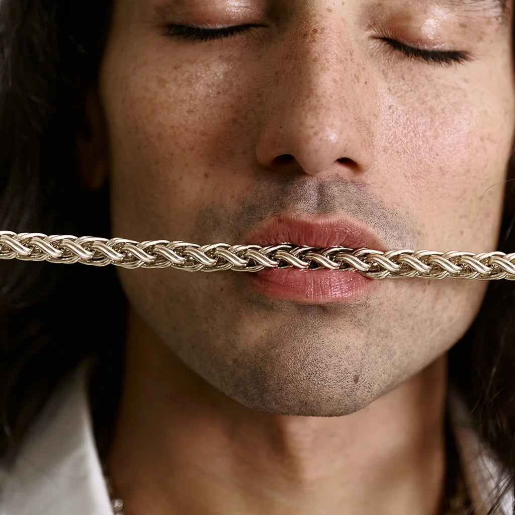 Un homme tenant le collier maille Anomalie en Chaine en métal satin doré en zoom.