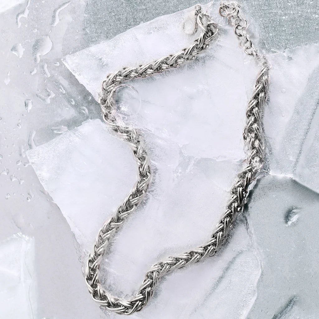Collier maille Anomalie en métal argenté, dont les maillons satinés captent parfaitement la lumière, posé sur un fond de glace.