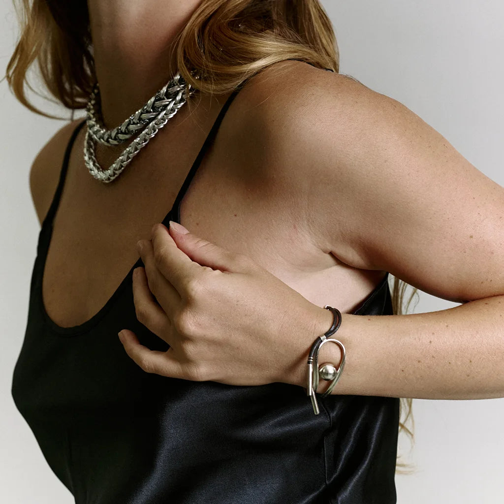 Une femme portant un bracelet perle original Anomalie en métal doré et cuir noir, accompagné de deux colliers tressés.