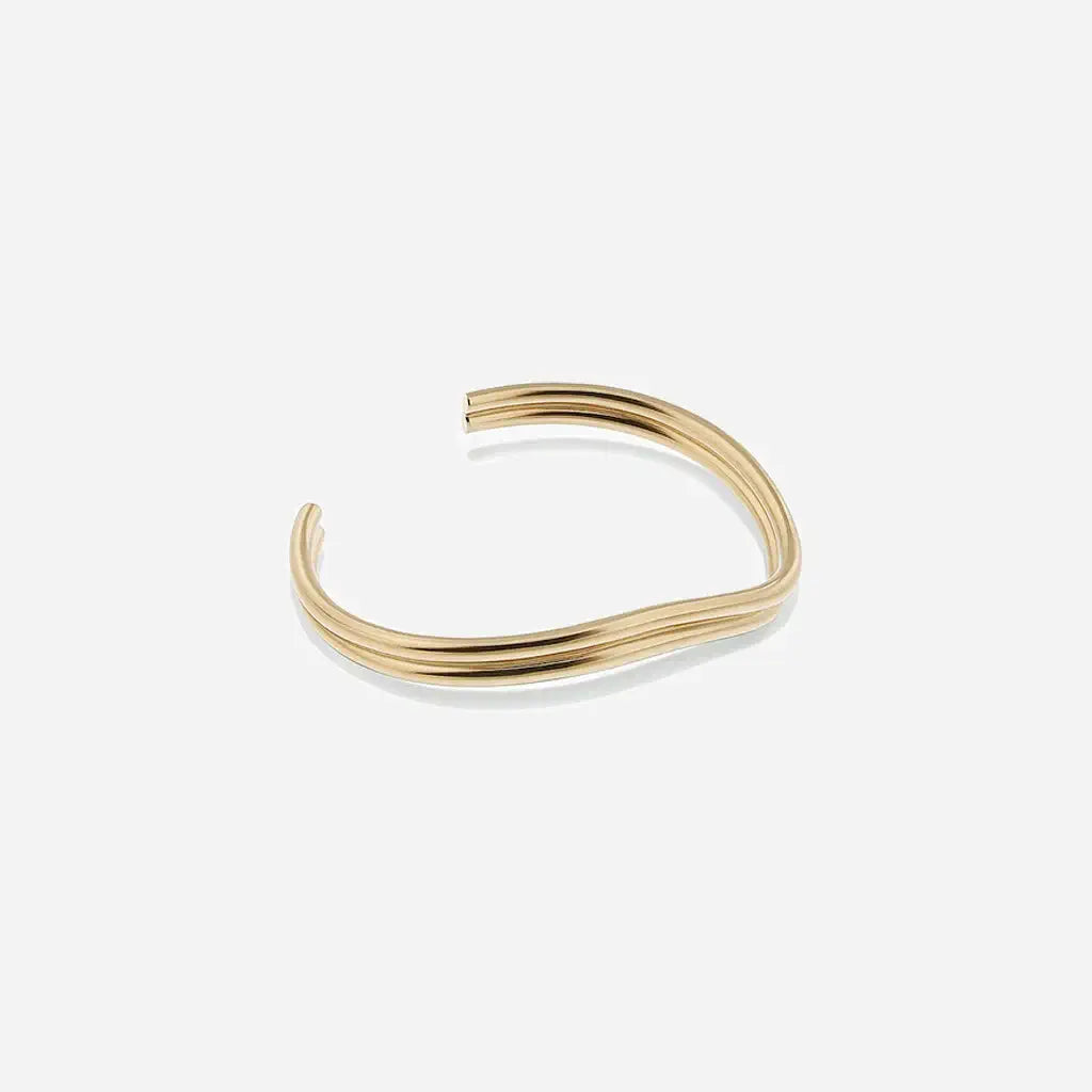 Jonc fin Anomalie, bracelet ouvert unisexe en métal satiné doré, à la fois ondulé, structuré et graphique.