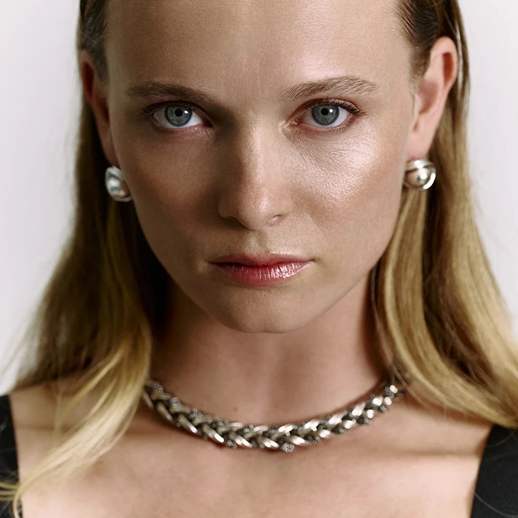 Visage d’une femme portant des boucles d’oreilles perles Anomalie en métal satiné argenté, avec collier assorti.