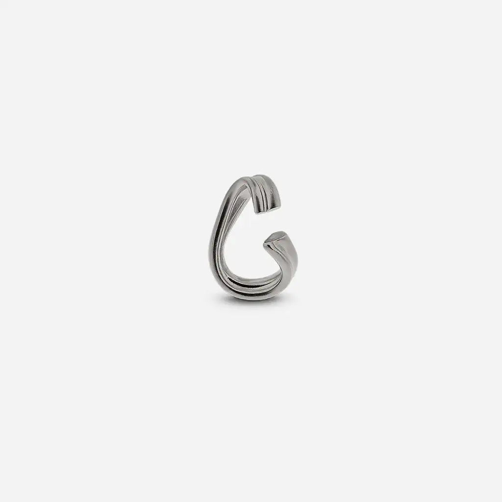 Bijou d'oreille Anomalie en métal satiné argenté, sculptural, avec une forme arrondie et légèrement torsadée.