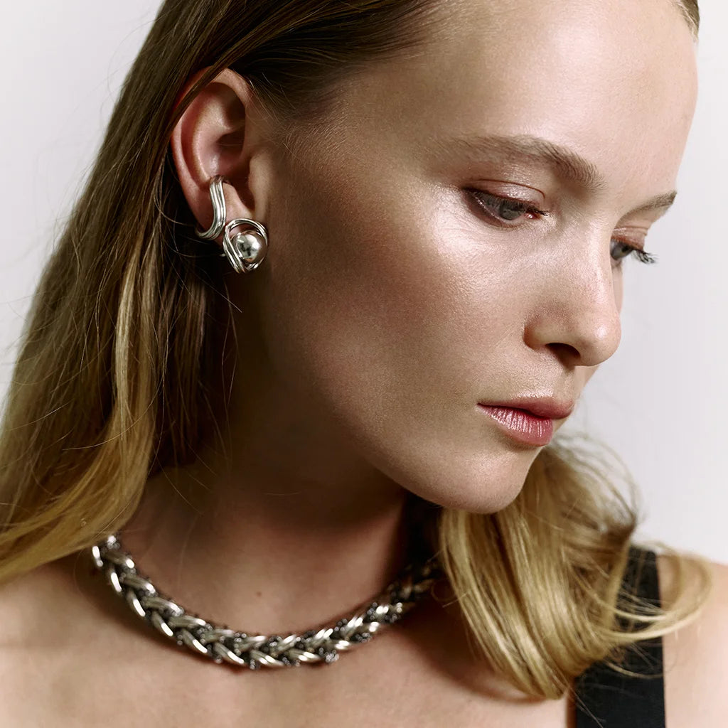 Une femme portant un bijou d'oreille Anomalie en métal argenté, avec des boucles d’oreilles perles et un collier assorti.