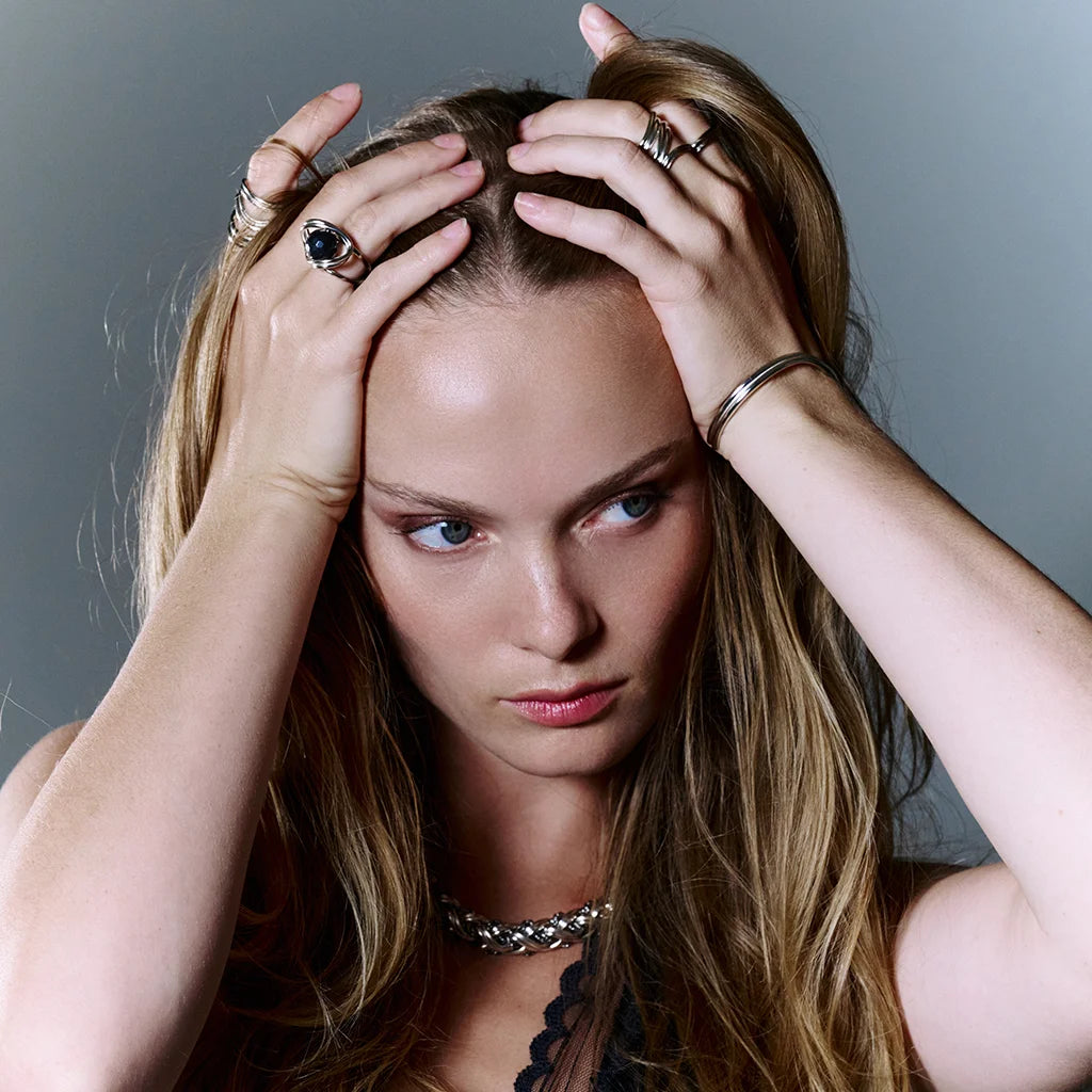 Une femme portant une bague perle moderne Anomalie en argenté assortie au jonc fin doré et d’autres bijoux.