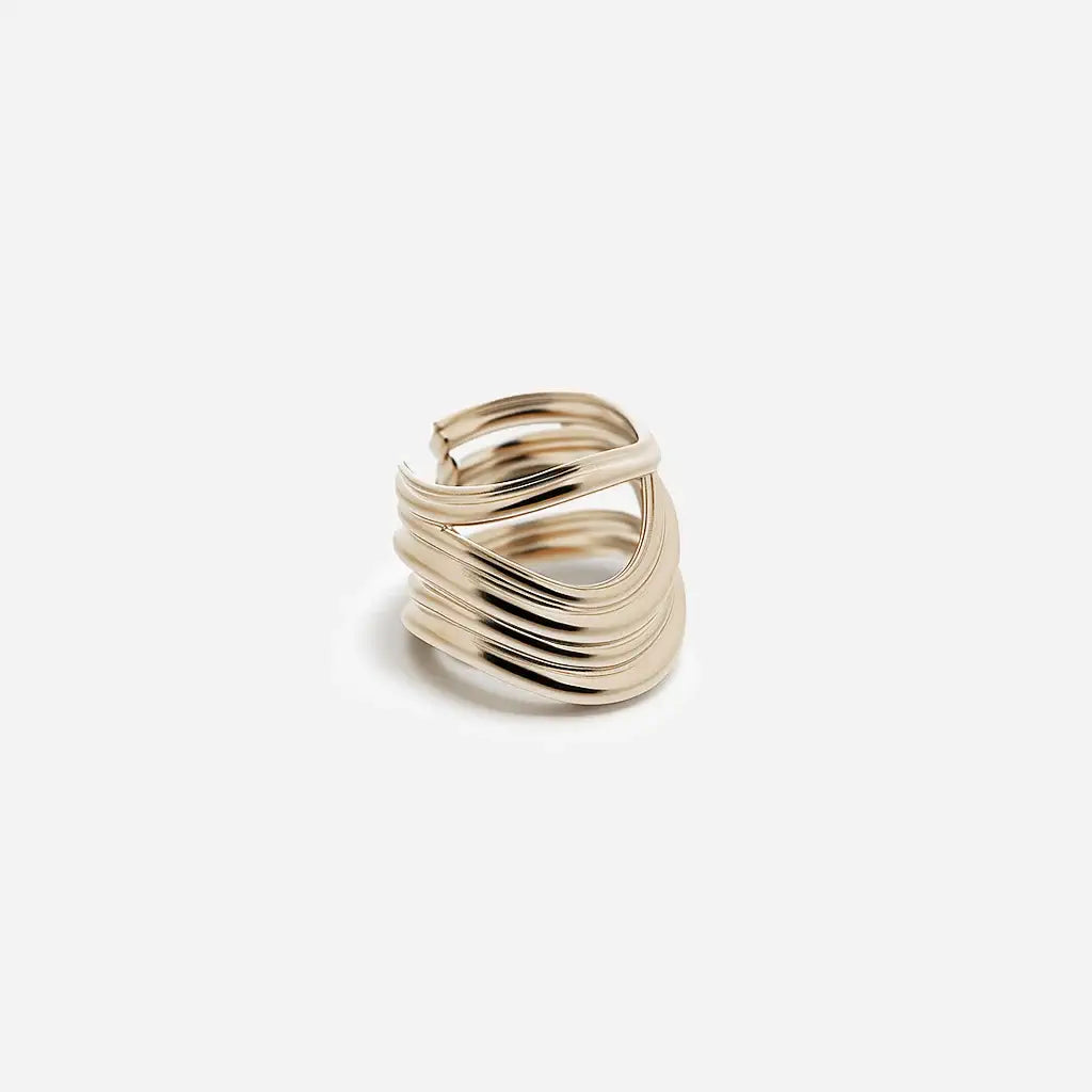 Une bague large Anomalie graphique en métal satiné doré, composée de plusieurs lignes métalliques volumineuses.