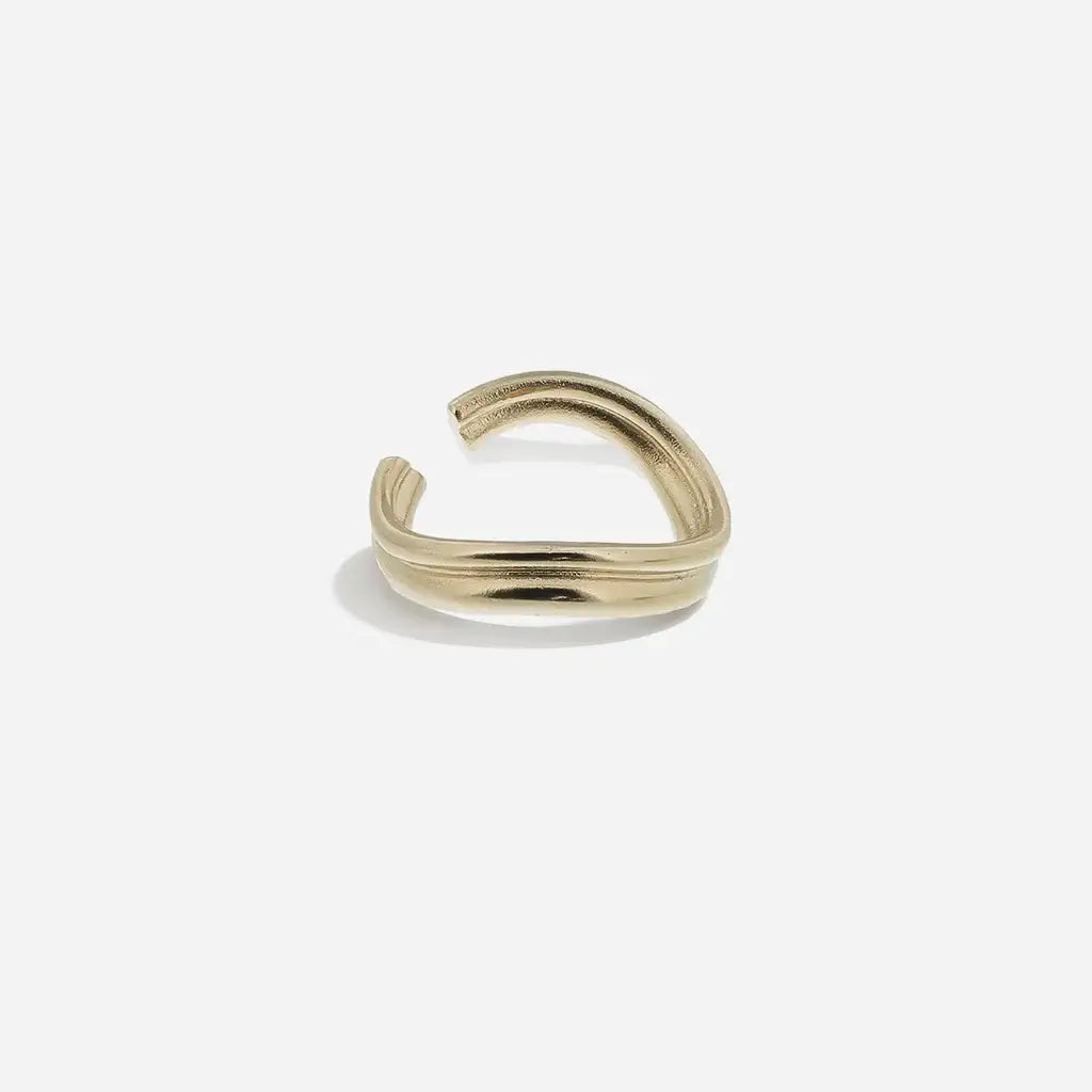 Bague ondulée Anomalie, graphique et ouverte, en métal satiné doré, avec une ligne fluide et minimaliste.