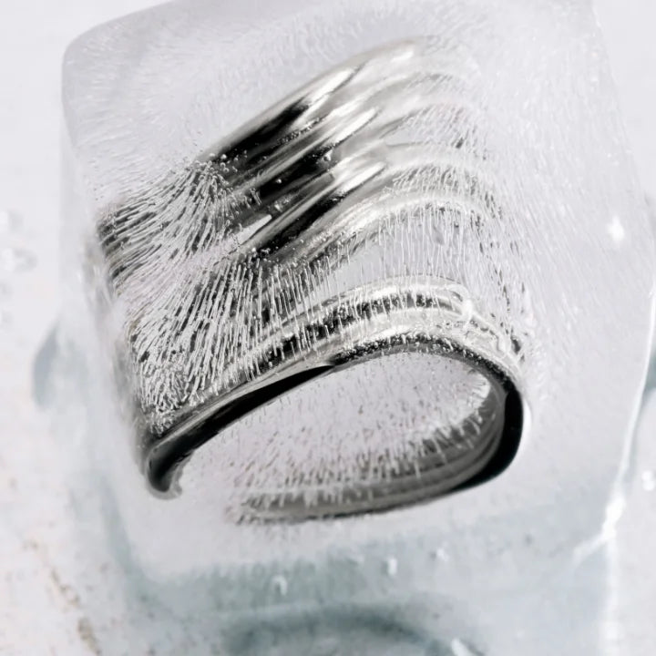 Une bague large homme Anomalie graphique en métal satiné argenté, posé en nature morte sur un glaçon.