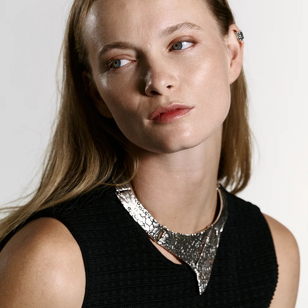 Une femme portant un collier torque Turbulence en vieil argenté, à structure rigide en métal, rehaussé de motifs texturés et finitions vieillies.