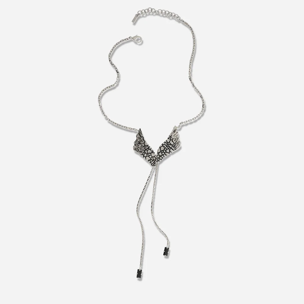 Un collier Ailes Trouble en vieil argenté orné de strass noirs, avec chaîne fine et pièce centrale articulée élégante.