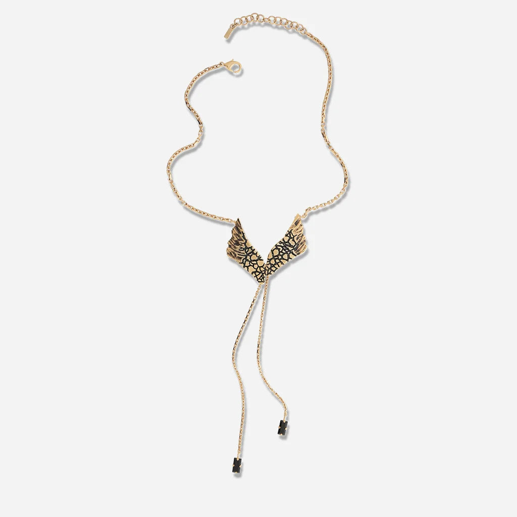 Un collier Ailes Trouble en vieux doré orné de strass noirs, sublimé par une chaîne fine et une pièce centrale articulée.