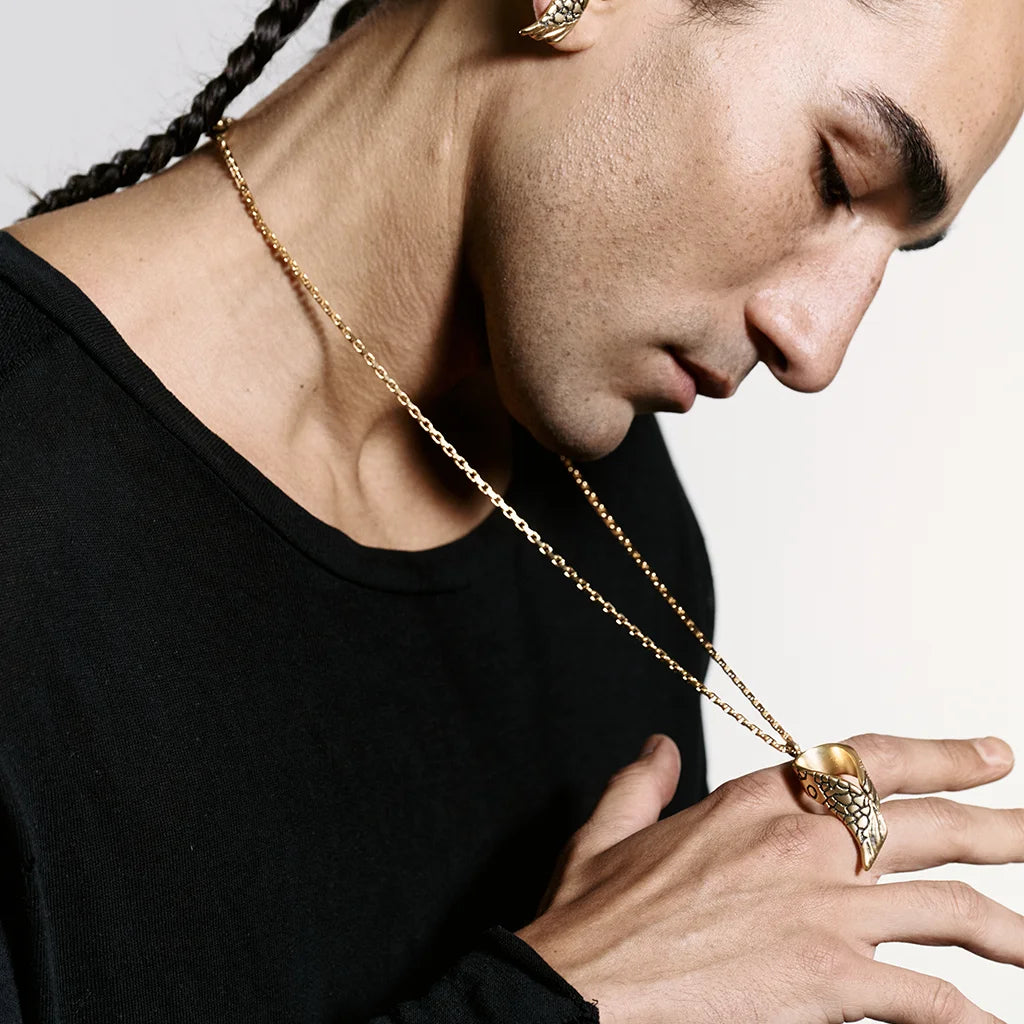 Un homme de profil portant autour du cou un collier pendentif Ailes Trouble en vieux doré, qu’il tient de la main.