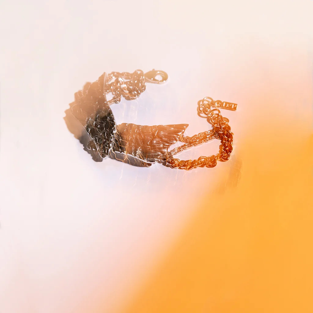 Le bracelet ailes Turbulence en vieil argenté texturé de fissures, avec sa triple chaîne, présenté sur fond coloré.