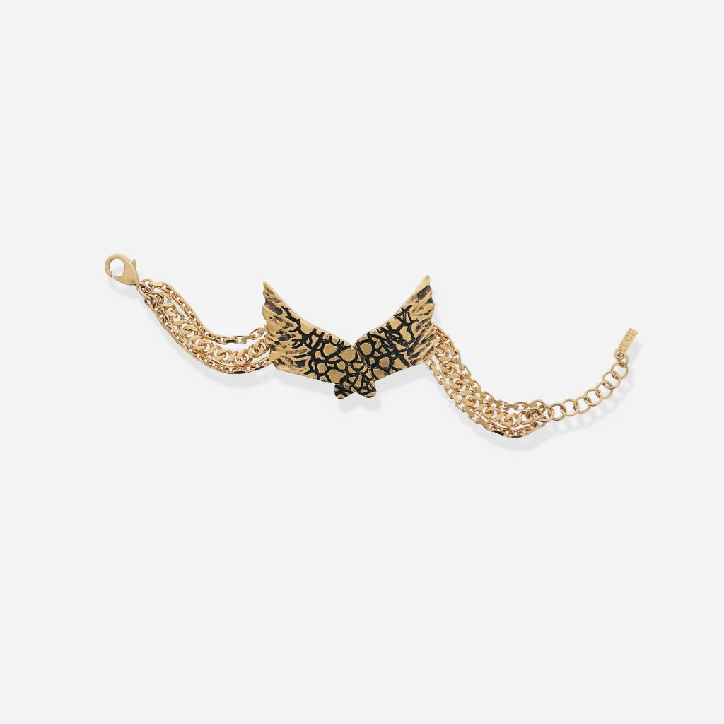 Le bracelet Ailes Trouble en vieux doré, gravé de motifs texturés, avec trois rangs de chaînes métalliques.