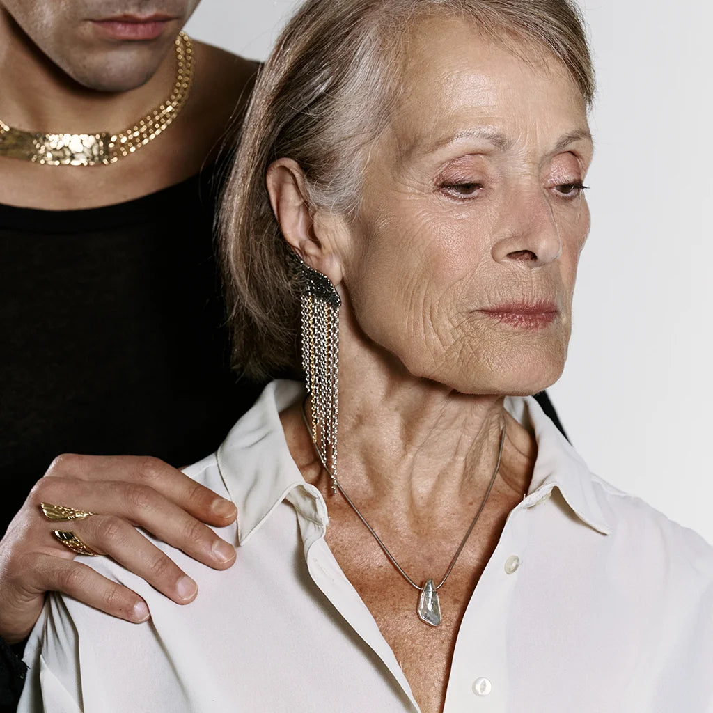 Une femme portant une boucle d’oreille originale créateur Trouble en vieil argenté avec mélange de chaînes dorées et argentées.