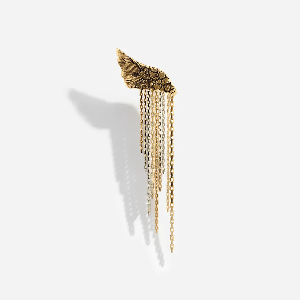 Une boucle d’oreille originale créateur Trouble en vieux doré, avec élément texturé en forme d’aile et tombé de chaînes bicolores.