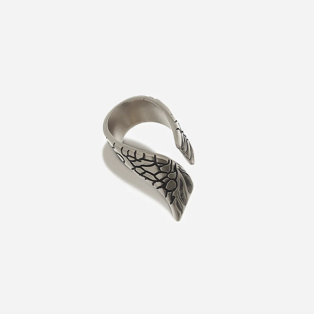 Une bague aile Trouble en métal vieil argenté structuré et ouverte aux lignes asymétriques, avec motif de l’aile.