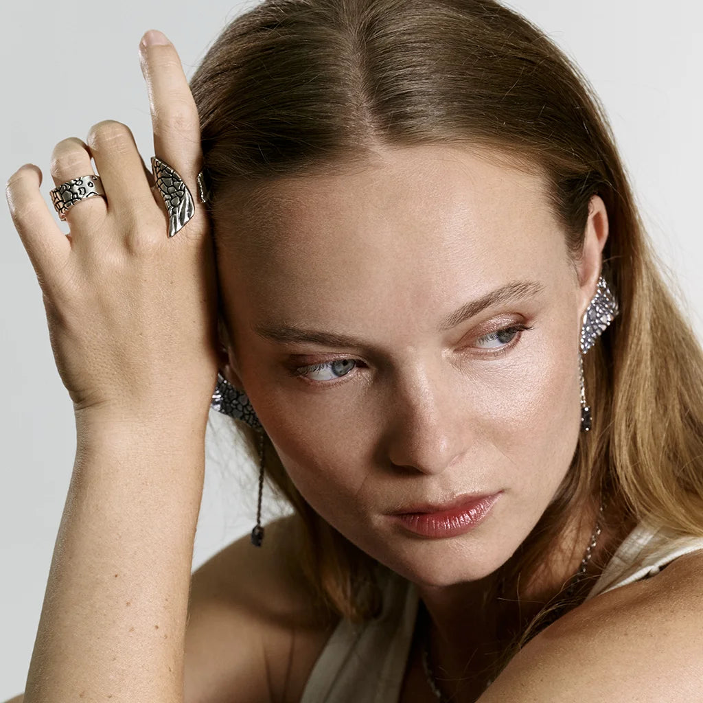 Une femme portant une bague texturée Trouble en métal vieil argenté, accompagnée d’autres bijoux Trouble assortis.