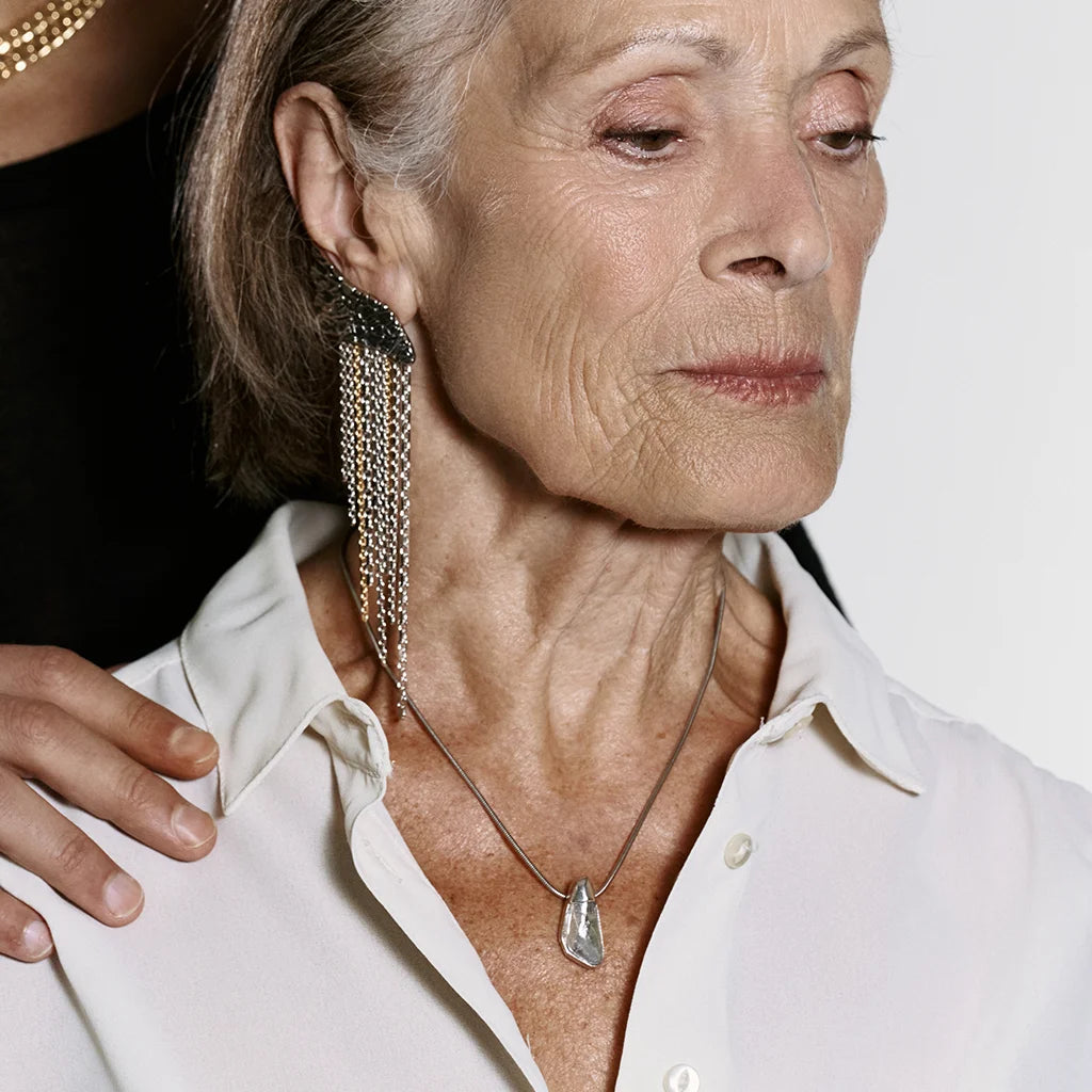 Une femme portant un petit collier Turbulence en métal argenté et une boucle d'oreille créateur Trouble.