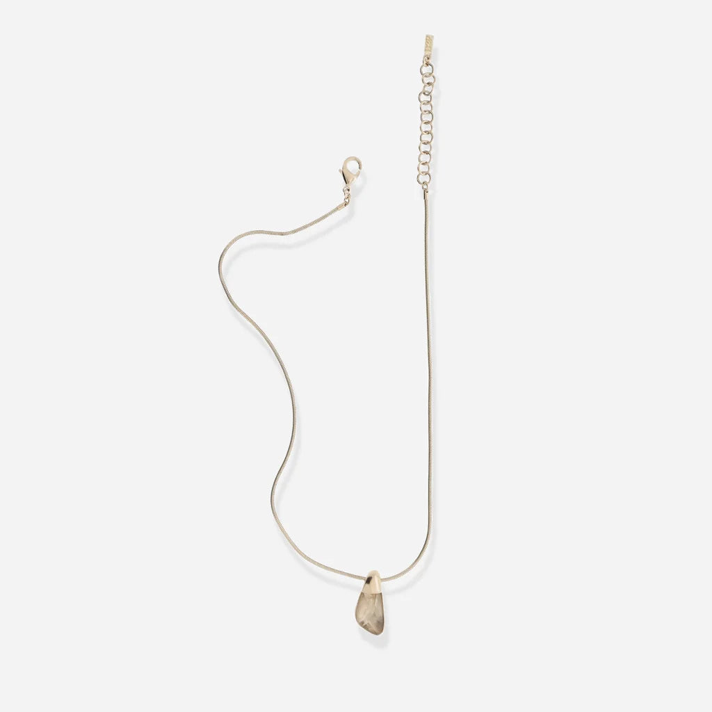 Le petit collier Turbulence en métal doré révèle son pendentif aux contours irréguliers et sa chaîne fine.