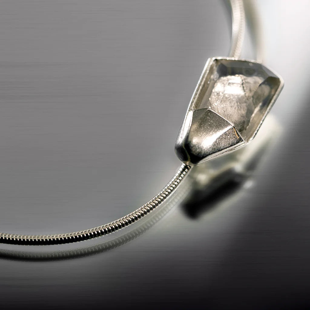 Sur un fond gris, est posé un bracelet cristal de roche Turbulence en zoom de couleur métal doré.

