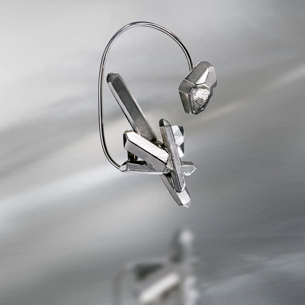 Sur un fond aluminium, reflète le bijou d'oreille créateur Turbulence en métal argenté pour femme.
