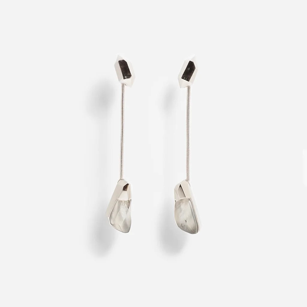 Les boucles d'oreilles cristal de roche Turbulence longues en métal argenté, suspendues à une chaine serpent fine.