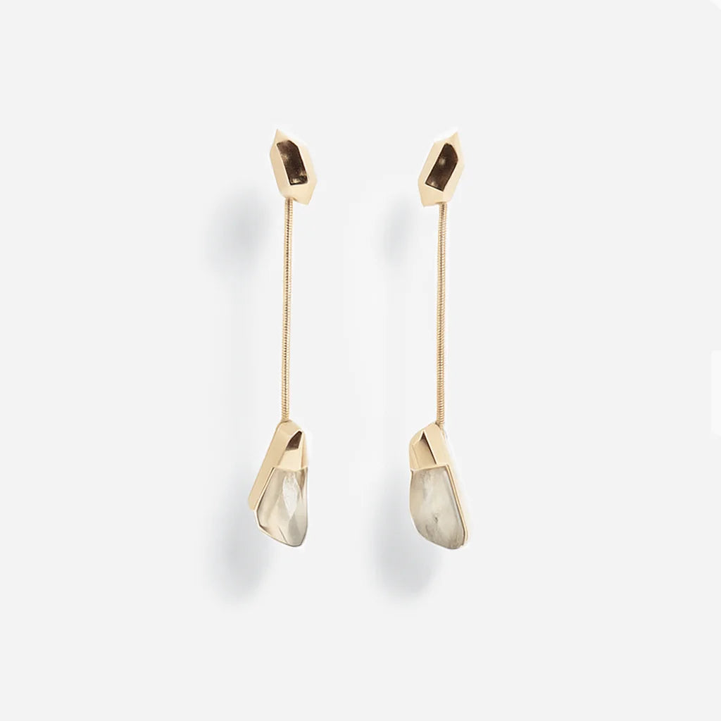 Les boucles d'oreilles cristal de roche Turbulence longues en métal doré, suspendues à une chaine serpent fine.