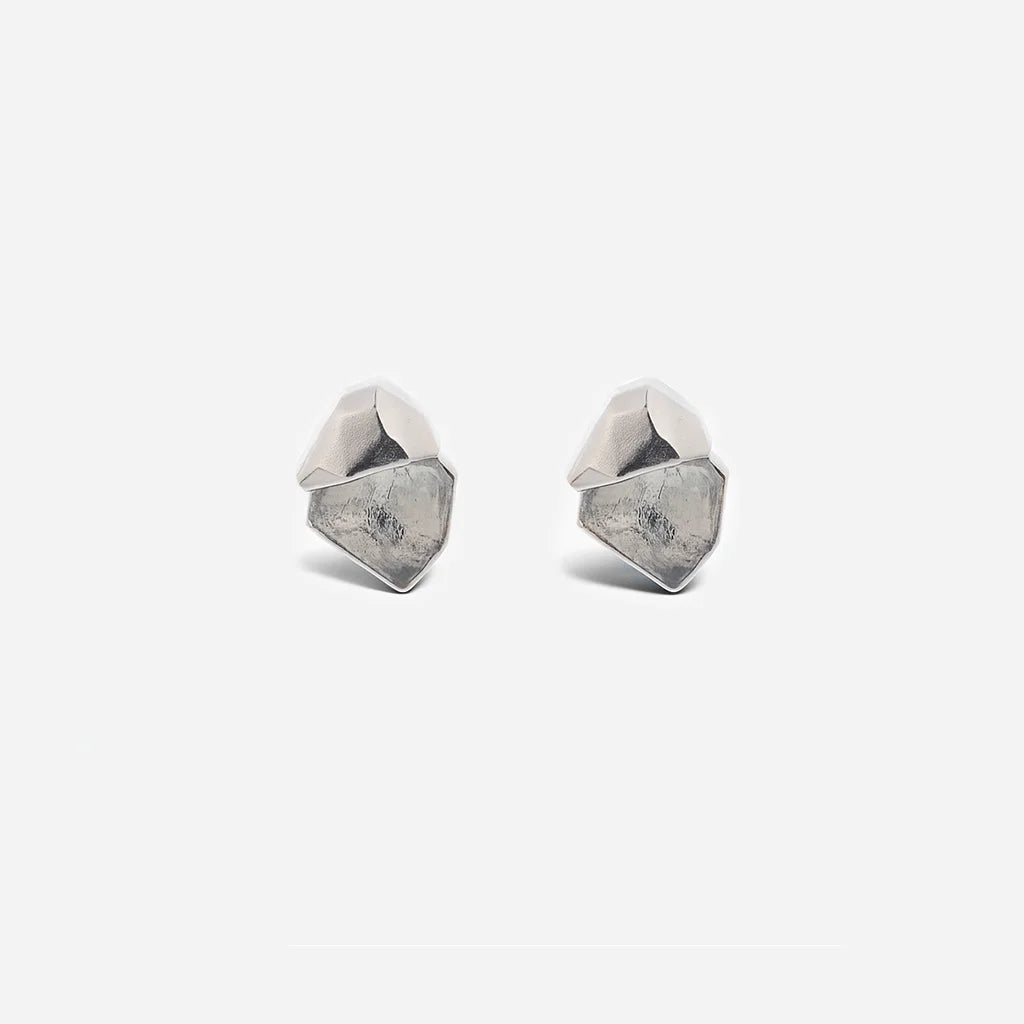 Des puces d'oreilles cristal de roche Turbulence en métal argenté, minimalistes et au design anguleux et graphique.