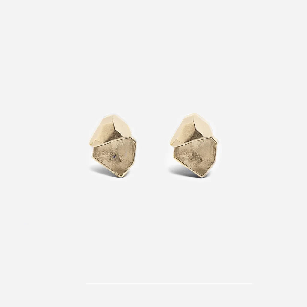 Des puces d'oreilles cristal de roche Turbulence en métal doré, minimalistes et au design anguleux et graphique.