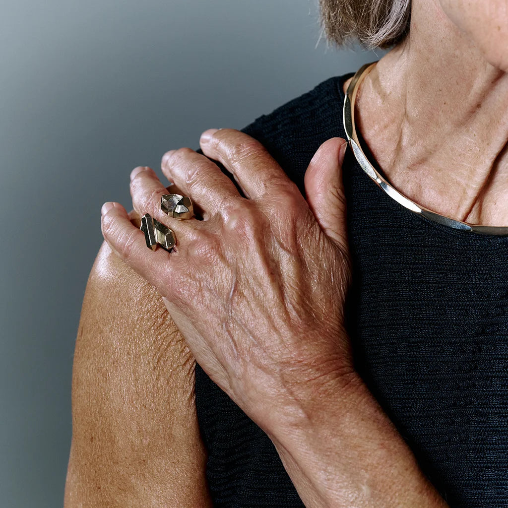Une femme portant une bague cristaux de roche Turbulence aux formes irrégulières en métal doré avec un collier torque.