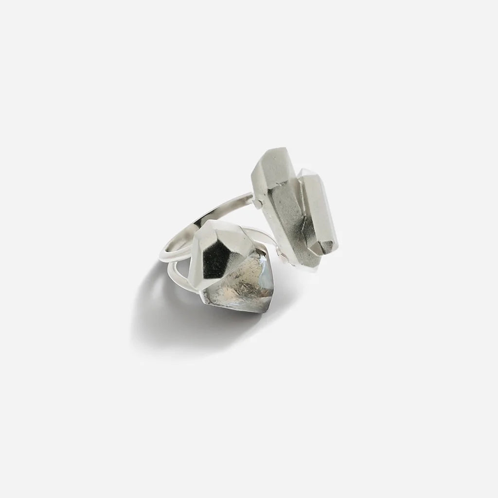 La bague cristaux de roche Turbulence en métal argenté rehaussée de deux cristaux aux formes irrégulières.